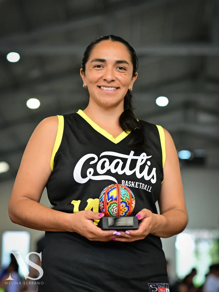 Diana Báez, con su uniforme de básquetbol, sosteniendo un trofeo de campeona